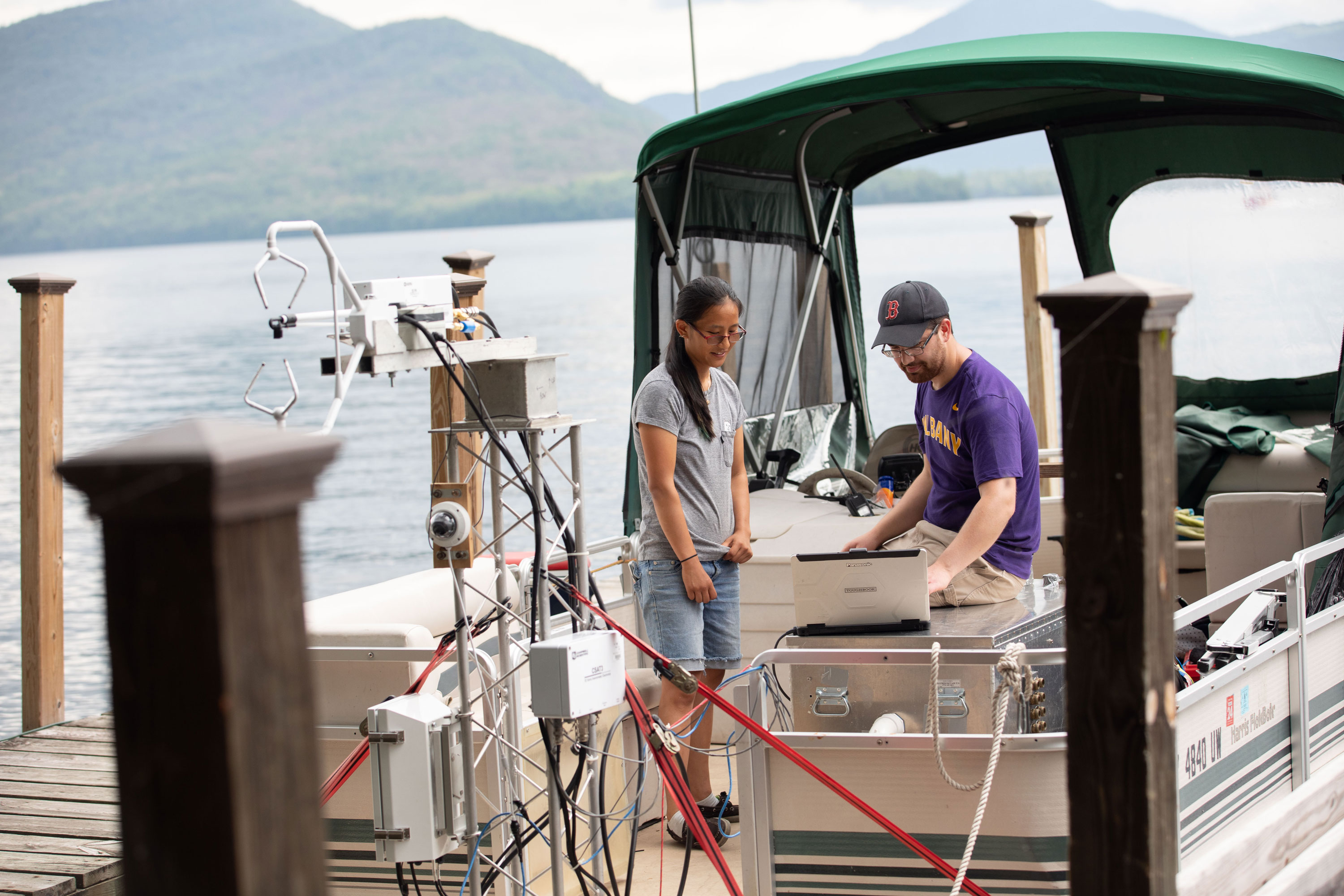 A graduate student and a researcher look at a computer monitor while taking measurements from a boat on Lake George.
